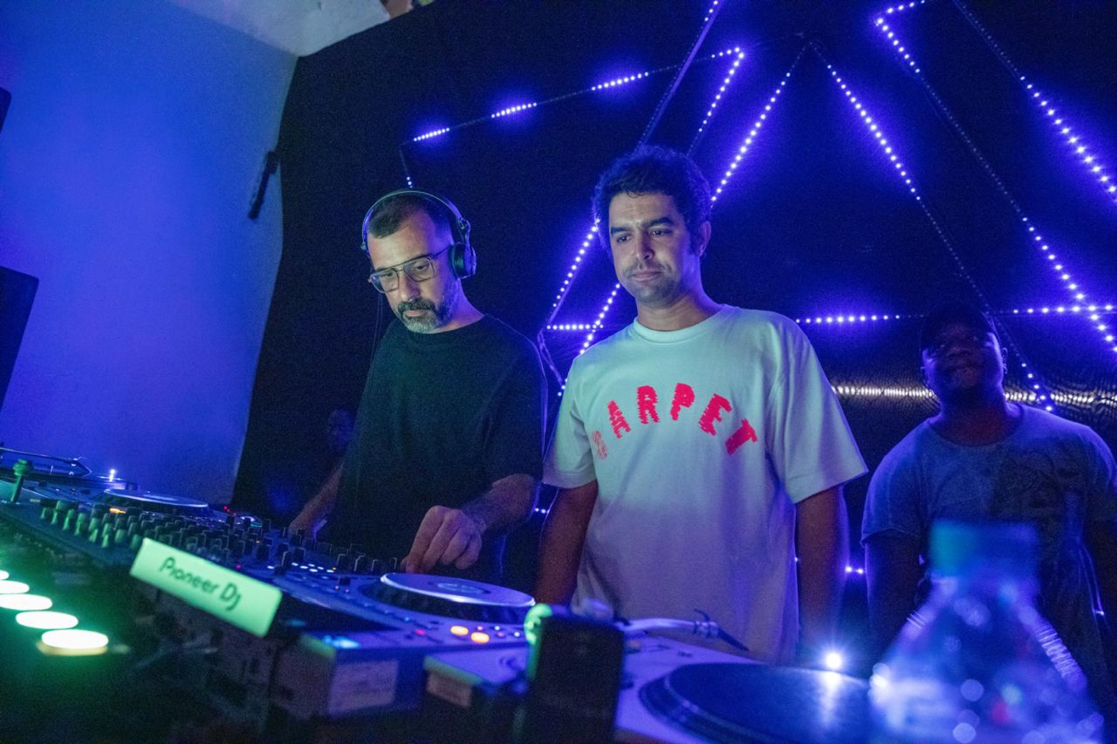 KULAS at the decks in a club under blue and magenta light.