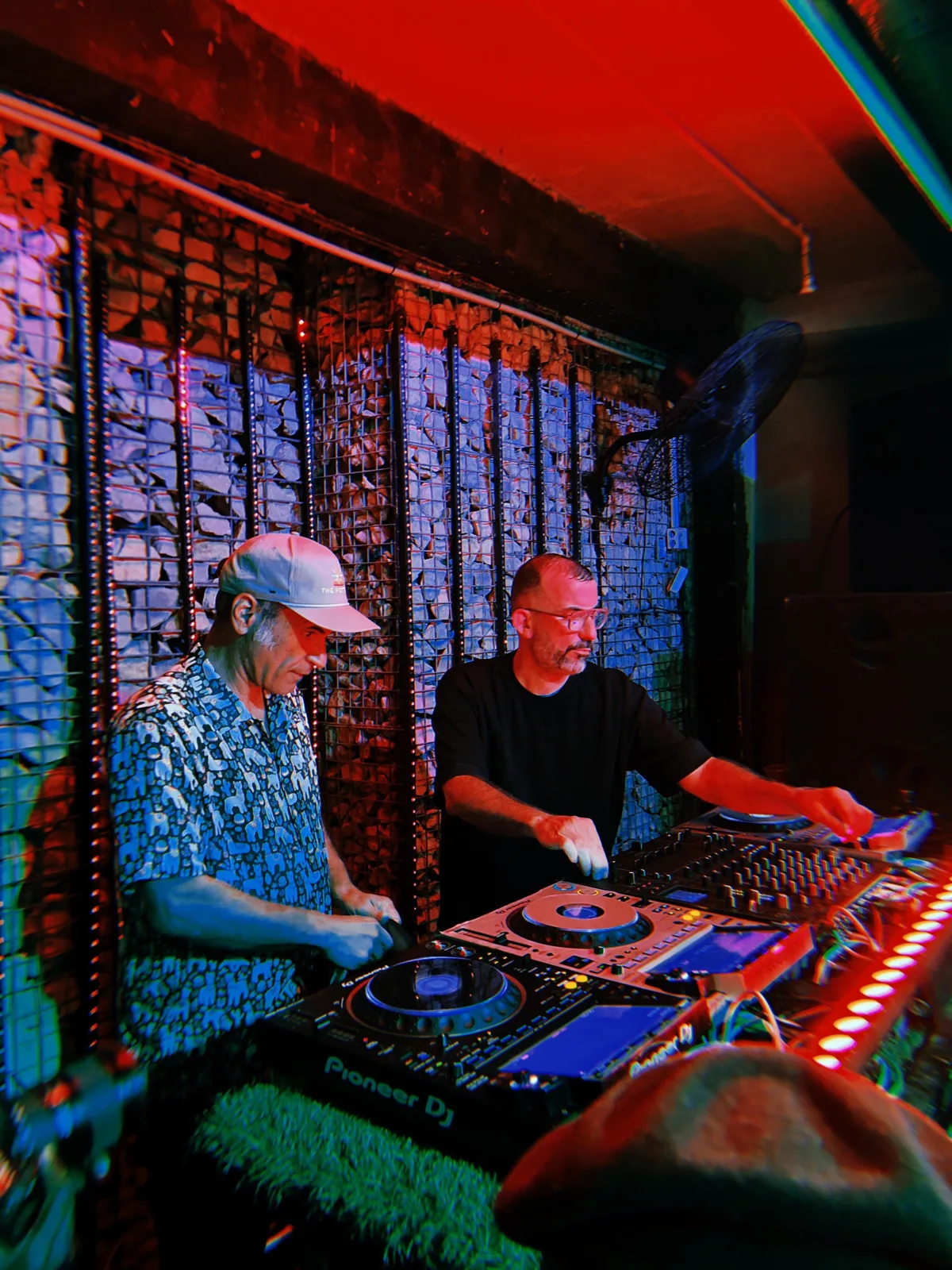 KULAS in a club booth with another artist under red and blue light.
